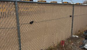IRONCLAD sensor cable mounted with clips along a chain link fence with privacy slats and barbed wire at a vehicle impound lot.