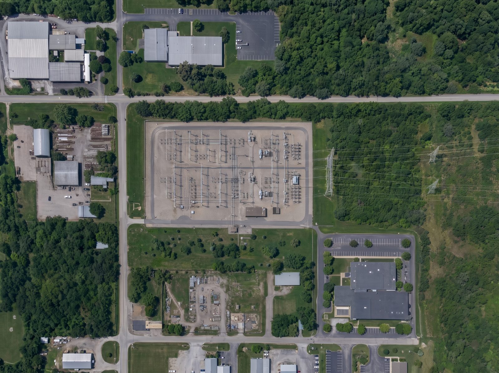 Aerial view of a high-voltage electrical substation with transmission lines and a fenced compound
