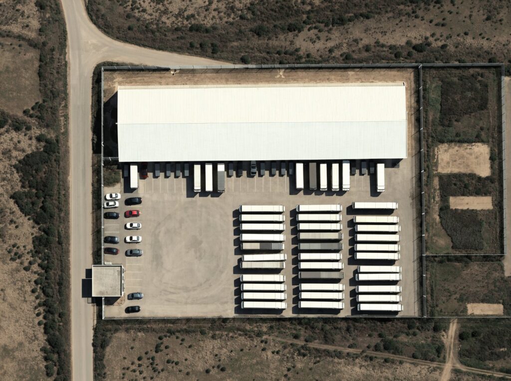 Aerial view of a fenced commercial distribution site with a warehouse, loading docks and a trailer yard