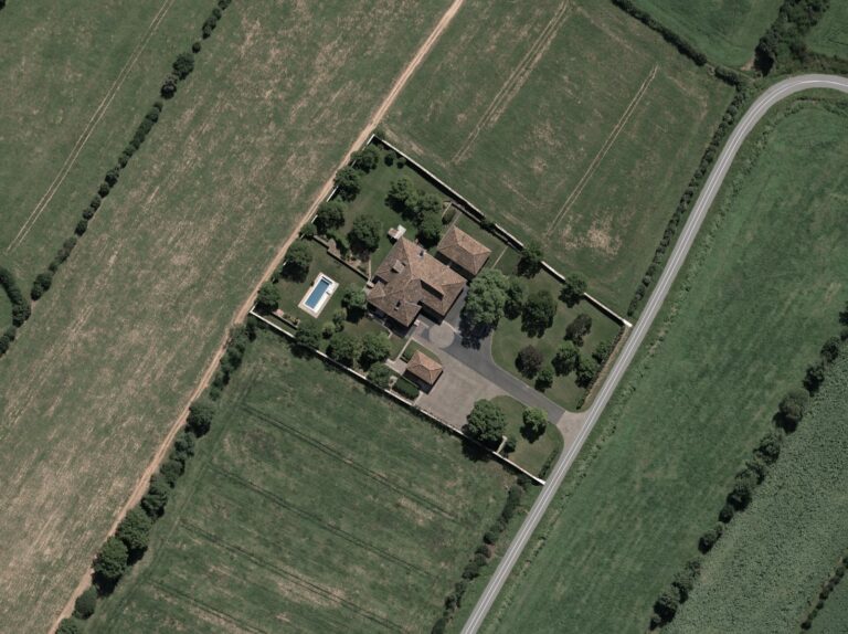 Aerial view of a walled private country estate with a gated driveway and surrounding farmland