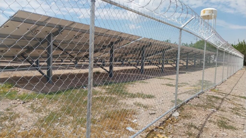 Chain link perimeter fence topped with concertina coil running alongside rows of solar panels at a solar park in northern Mexico.